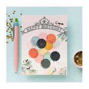 Birds sitting on pine branches looking at colorful transparent balloons birthday card